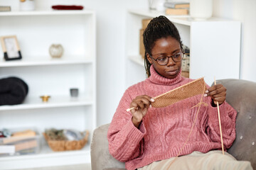 Portrait of young African-American woman knitting at home while enjoying cozy weekend, copy space