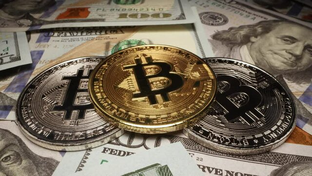 Gold Bitcoin placed on silver cryptos stacked on top of 100 dollar bills while slowly turning in macro view.
