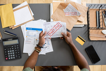 High angle view of unrecognizable blackman sitting at table with bills and checking arrears of...