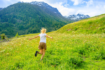Fototapeta na wymiar carefree woman with a short skirt running in the countryside of Guarda village of Scuol municipality in Switzerland. Guarda town by the River Inn of Swiss canton Grisons.