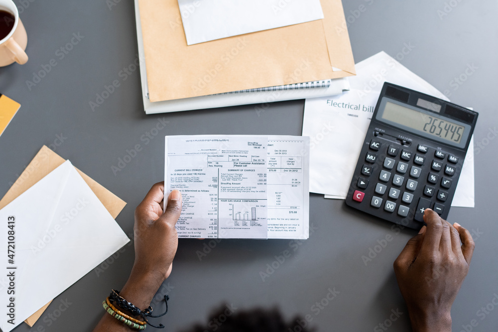 Poster Directly above view of blackman sitting at gray table with letters and making calculations while examining bills