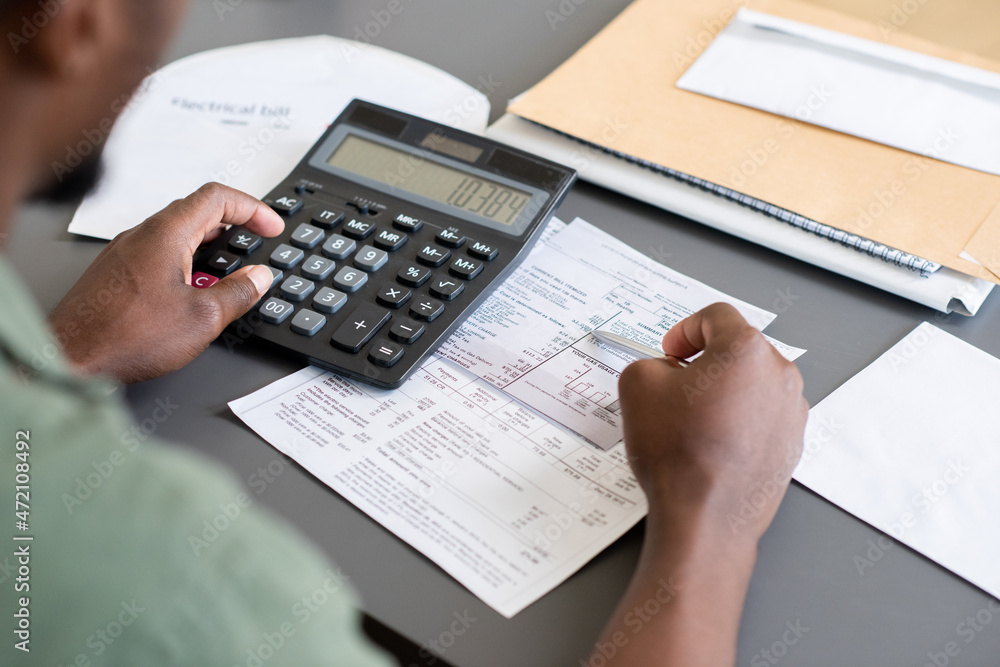 Poster Close-up of unrecognizable blackman sitting at table and checking bills while calculating personal finances