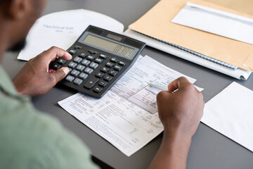 Close-up of unrecognizable blackman sitting at table and checking bills while calculating personal finances