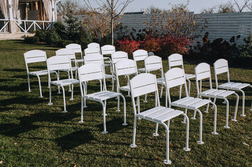 A set, a row of white wooden chairs stands on green grass in a park in nature. Wedding photography.