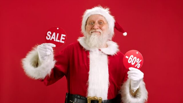 Christmas SALE -60 Off. Cheerful Santa Claus is Dancing and Joyful From Christmas Sale Holding Two Banners With Inscription SALE and -60 Off Showing Off Inscriptions to Camera on Red Background.