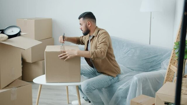New house owner Middle Eastern man is opening cardboard boxes unpacking belongings during relocation. Household and young people concept.