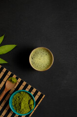 matcha green tea with foam, powder from ground tea leaves in a bowl on a black background. Top...