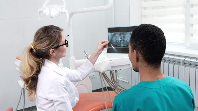 Caucasian female dentist explaining to student x-ray. Cabinet equipment on background