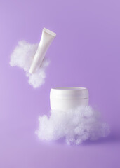 Facial cream and lip balm with fluffy clouds on violet background. Concept care with sensitive...