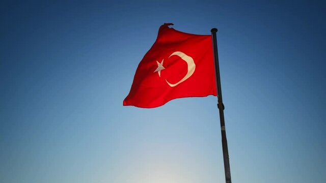 Turkish red flag with white star and crescent is waving on the wind in slowmo filmed from above. A national symbol of one of famous touristic country is rippling in the air with blue sky on background