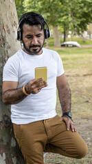 Latino man leaning against a tree looking at his yellow cell phone