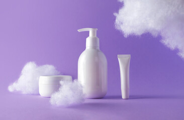 Cosmetic set with fluffy clouds on violet background. Beauty products bottles for skincare or body...