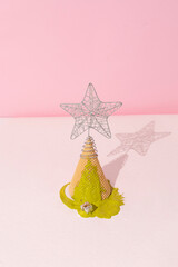 Christmas tree made of ice cream cone with star bauble on top and pistachios green spilled paint. Pink pastel colored background, close up perspective. Christmas and new year celebration concept.