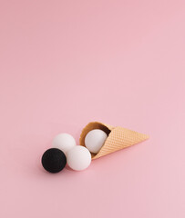 Ice cream cone with white and black christmas baubles under soft light on pastel pink background. Embracing racial diversity concept, close up composition.