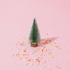 Christmas tree with confetti and multicolored party decoration on pastel pink background. Christmas and new year celebration concept. Close up perspective, square ratio.