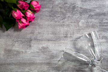 Decorative composition on grey wooden surface with roses and transparent wine glasses filmed from above. Romantic greeting card with bouquet of flowers. Preparing surprise for celebrating a love event