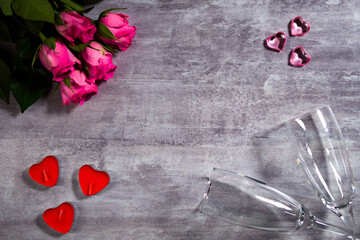 Festive background with roses and heart shape candles next to couple of wineglasses. Holiday decorative still life made of flowers and beads for romantic event. Valentine's Day and engagement concept.