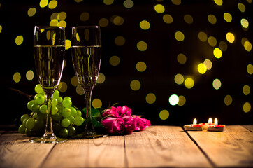 Closeup of a table prepared for spending romantic evening with champagne and burning candles. Still life made of wine glasses and fruit with pink roses on bokeh background. Celebrating Valentines Day.
