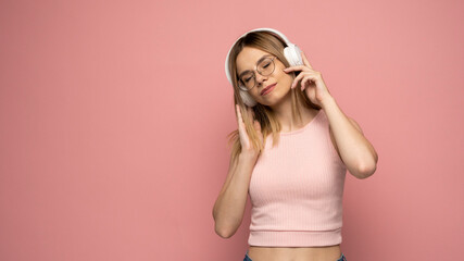 Lifestyle Concept. Portrait of beautiful woman in a glasses and pink shirt joyful listening to music. Pink studio background. Copy Space.