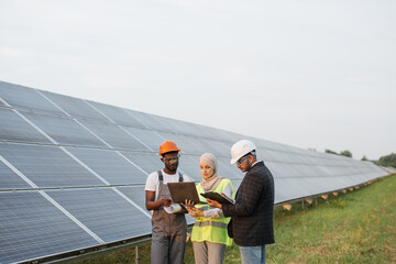 Muslim woman in hijab and indian man in white helmet talking with african american technician on...