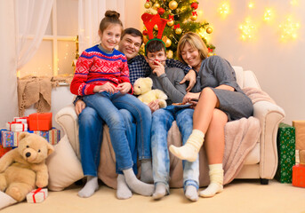 Winter holiday concept - Family sitting on a couch, interior with new year or christmas decoration. Children and parents. Holiday lights and gifts, Christmas tree decorated with toys.