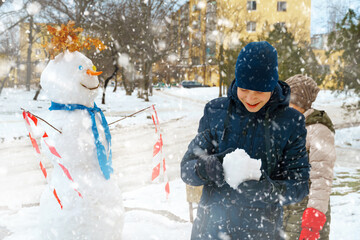 a girl and boy play with snow on a city street and make a snowman