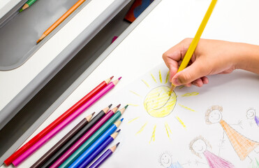 The child holds a yellow pencil in his hands and draws the sun. Children's education concept.