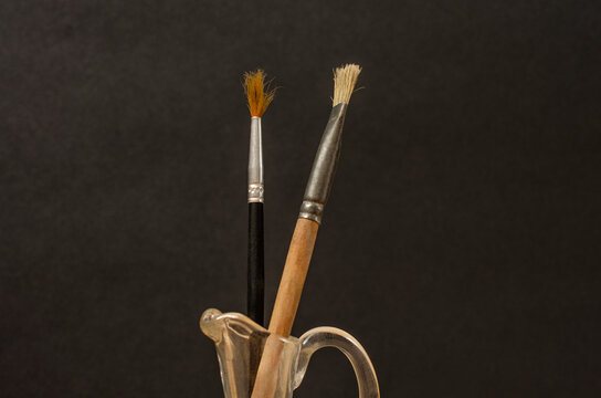 Old used artistic painting brushes in a terto glass vase. Still life. Minimalist composition with a black background.