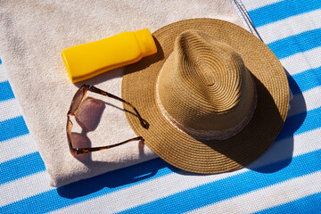Yellow sunscreen cream bottle for skin protection, sun glasses, straw hat and beach towel on the...