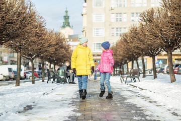Fototapeta na wymiar Two children talk and walk down the street in winter jackets and warm hats.