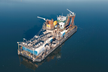 A floating platform with a huge bucket and conveyor belt extracts sand from the bottom of the...