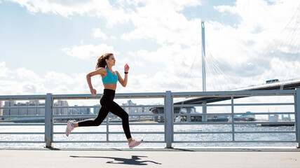 A sporty lifestyle, the coach does physical exercises.  Woman running city embankment, athletic figure, comfortable fitness clothes.