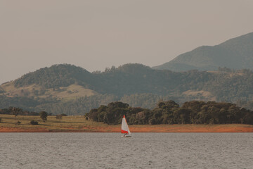 sailboat in the middle of a caml lake wiht mountains in the background