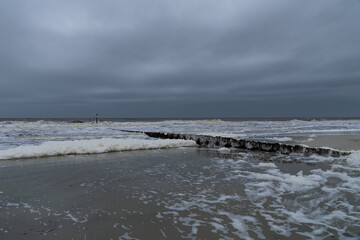 Dark skies and rough surf with an abundance of sea foam along a metal erosion control wall, South...