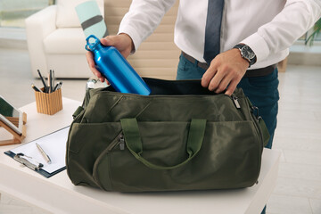 Businessman packing sports stuff for training into bag in office, closeup