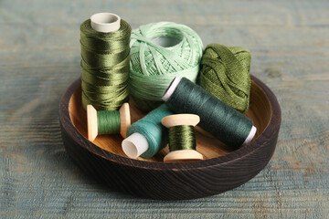 Fototapeta na wymiar Color sewing threads in bowl on light blue wooden table