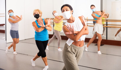 Women of different ages in face masks dancing together during their group training.