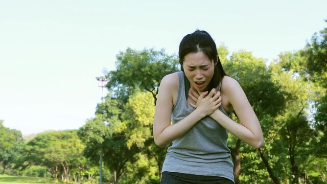 Woman exercising outdoors has chest pain, acute heart attack : Young woman suffering from heart disease holds her chest in agony.