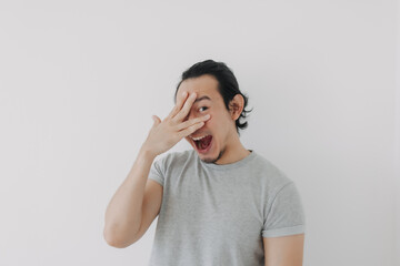 Funny cute shy Asian man in grey t-shirt on isolated white background.