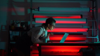 Young entrepreneur fashion designer work in studio at night communicating with clients of online shop using laptop or creating new social media marketing strategy for own brand of clothes development