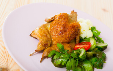 Delicious quail-tobacco with boiled and fresh vegetables and herbs at plate