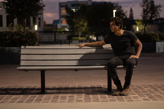 Boy Sitting Sideways At Night On A Bench Relaxed Looking Sideways To The Left Wearing Black Clothes