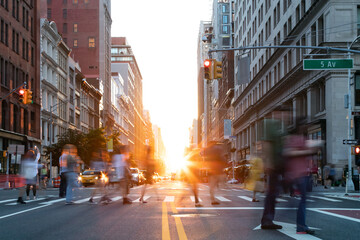 Busy street scene is crowded with people at an intersection on Fifth Avenue in New York City with sunlight shining between the buildings