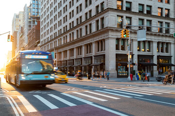 Busy street scene with people, bus and taxi at the intersection of 23rd and 5th Avenue in New York City with sunlight background