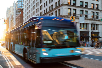 New York City bus driving down 23rd Street through Manhattan with sunlight shining between the...