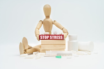 A figurine of a man sitting among pills lifts a red wooden block with an inscription STOP STRESS...