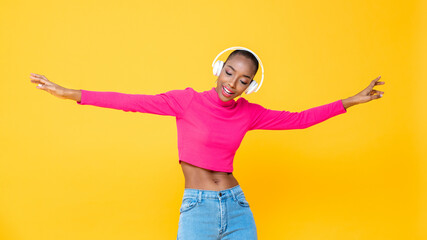 Portrait of happy African American woman wearing headphones listening to music and dancing on colorful yellow isolated background