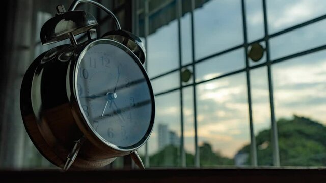 An alarm clock turning into 5 o'clock in the evening with beautiful sunset view outside the window