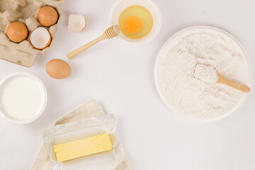 bread concept a stick of butter, a small bowl of raw egg, a plate of flour with a wooden spatula on it being on the light background