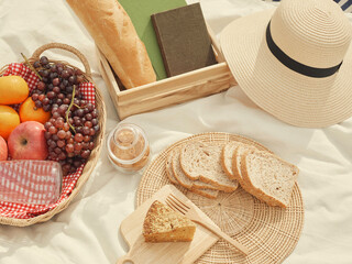 picnic concept There are a lot of things on the white cloth such as bread, fruits, a bottle of water, a hat and a notebook